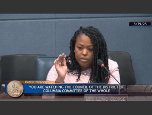 Photo of CM Janeese Lewis George on the dais at the Committee of the Whole hearing on May 29, 2025. She is wearing a pink checkered suit with pearl buttons.